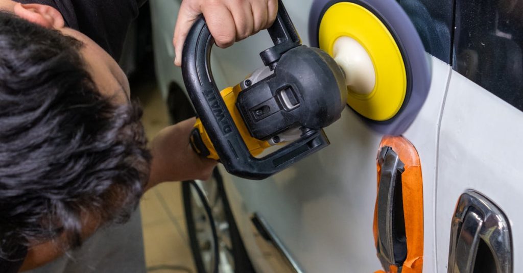 A man uses an electric buffer to polish and clean a white car door in a garage setting.