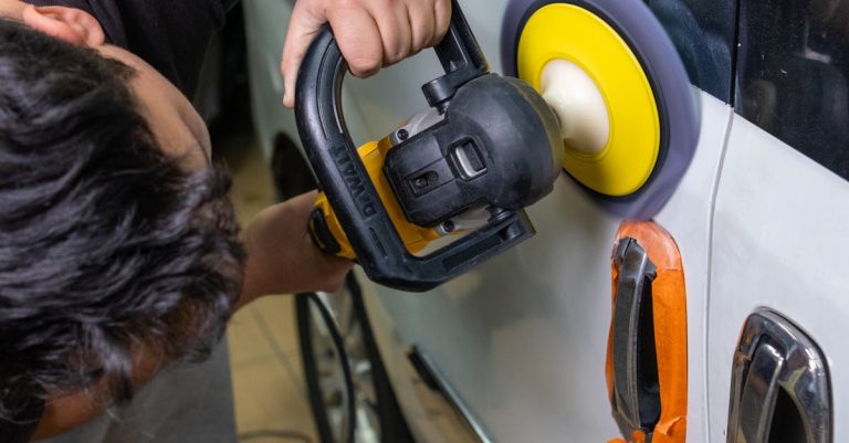 A man uses an electric buffer to polish and clean a white car door in a garage setting.